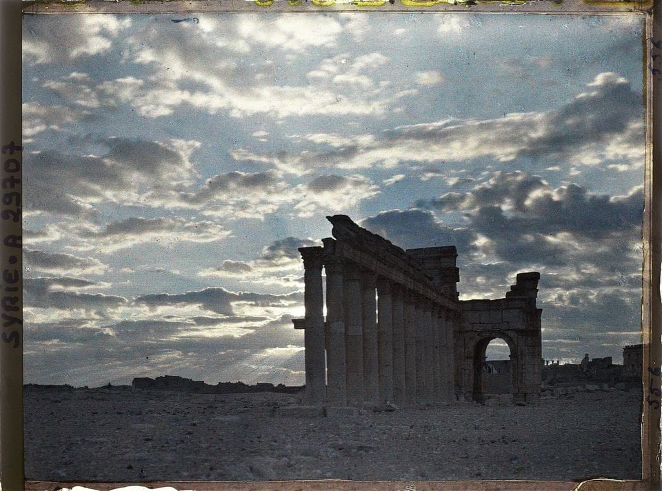 Silhouette of a ruined stone colonnade and arch against a cloudy sky