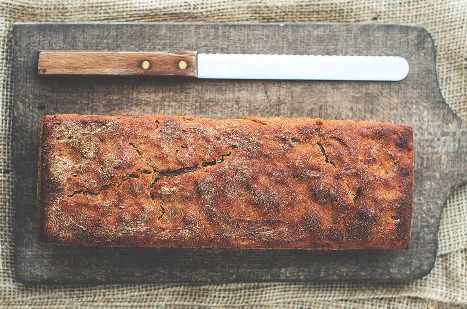 Loaf of dark bread on a wooden board with a serrated knife