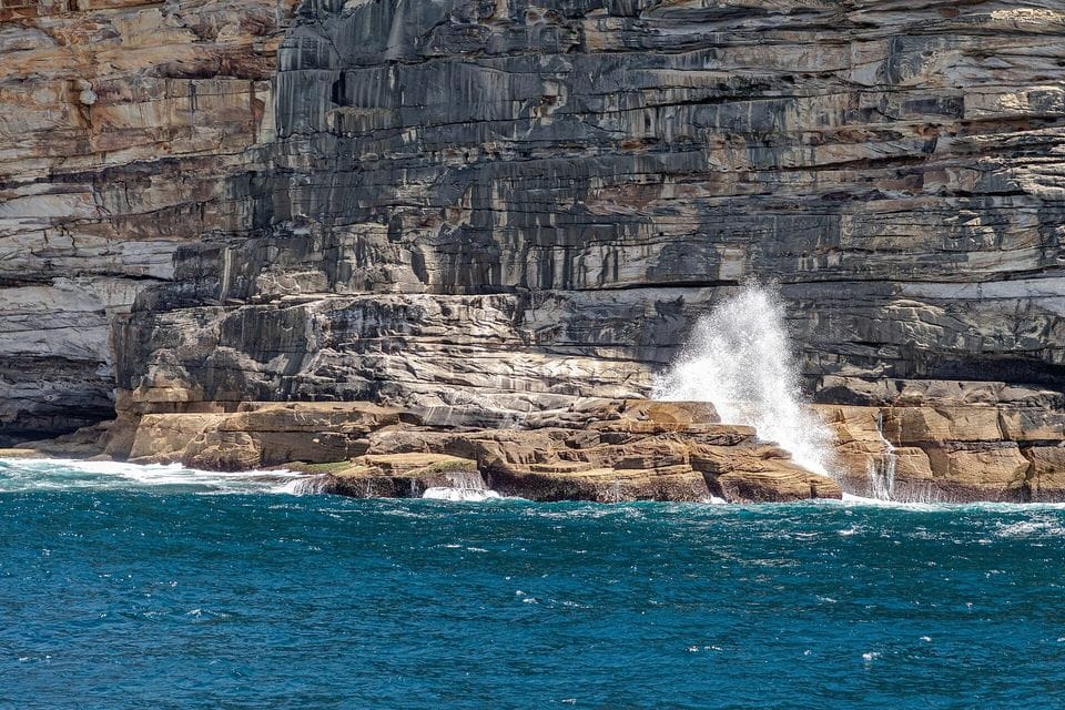 Layered sandstone cliff with a wave breaking at its base