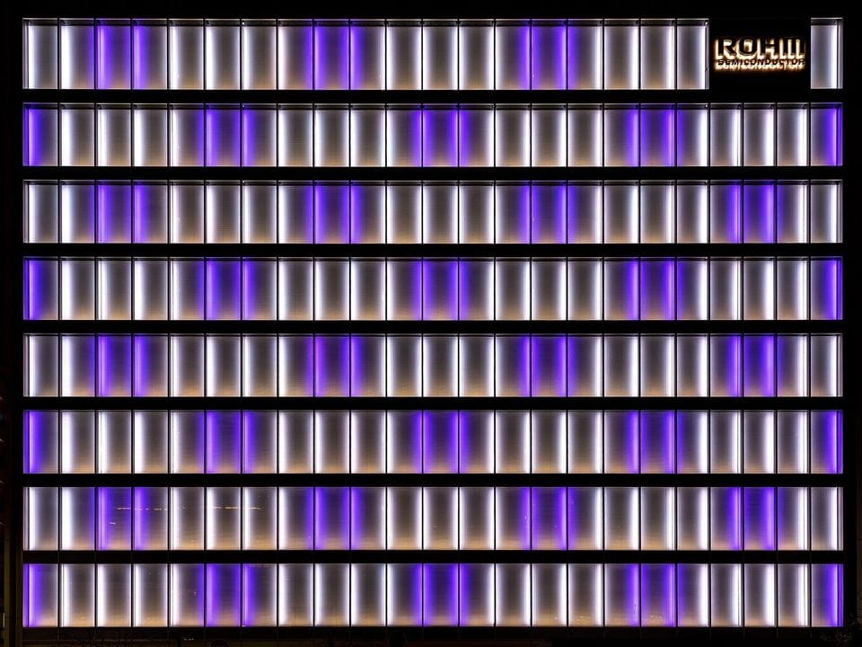 Office facade of repeating vertical panels lit in violet
