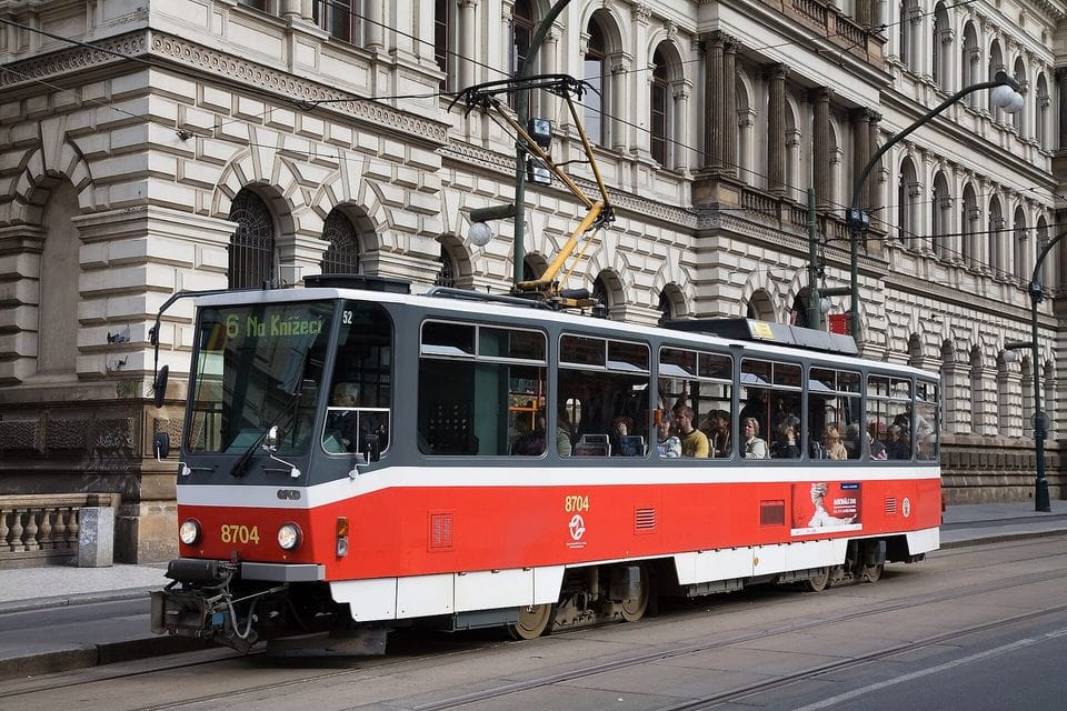 Red and white tram passing a stone building in a city street